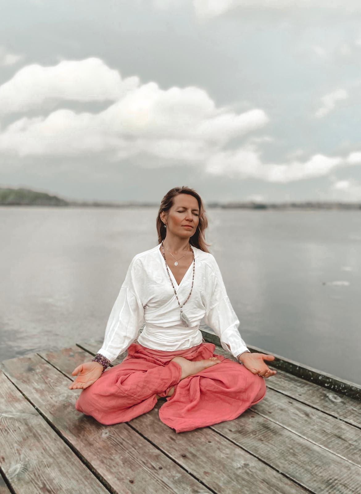 Kobieta siedzi na pomoście i medytuje, joga kundalini.